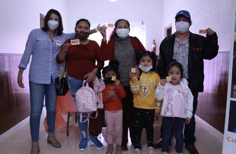 Four adults wearing masks and three young children pose and smile for a picture with their vaccine stickers