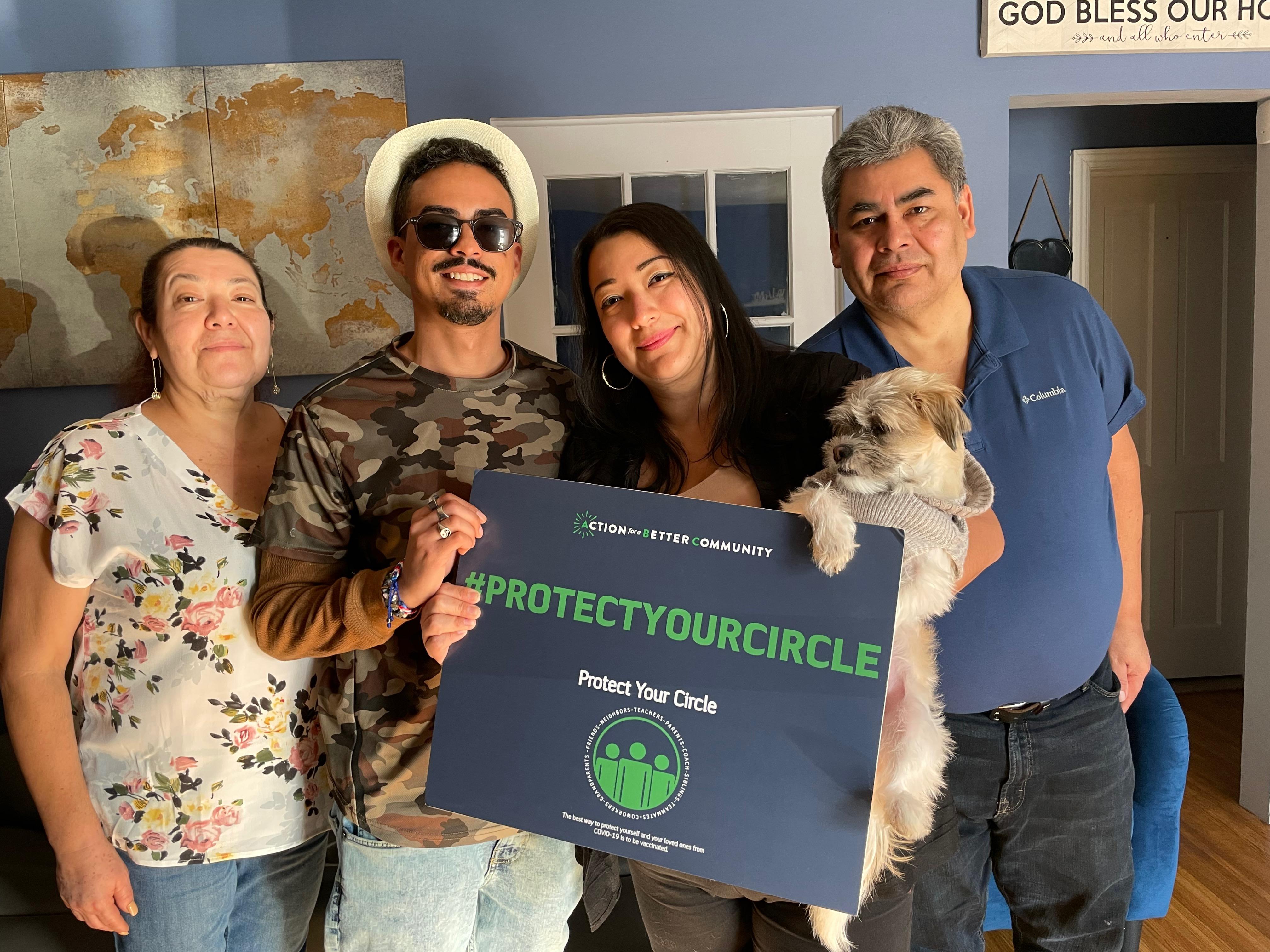 A group of people smile and pose for a picture. Two people in the middle hold a navy blue sign that says "protect your circle"