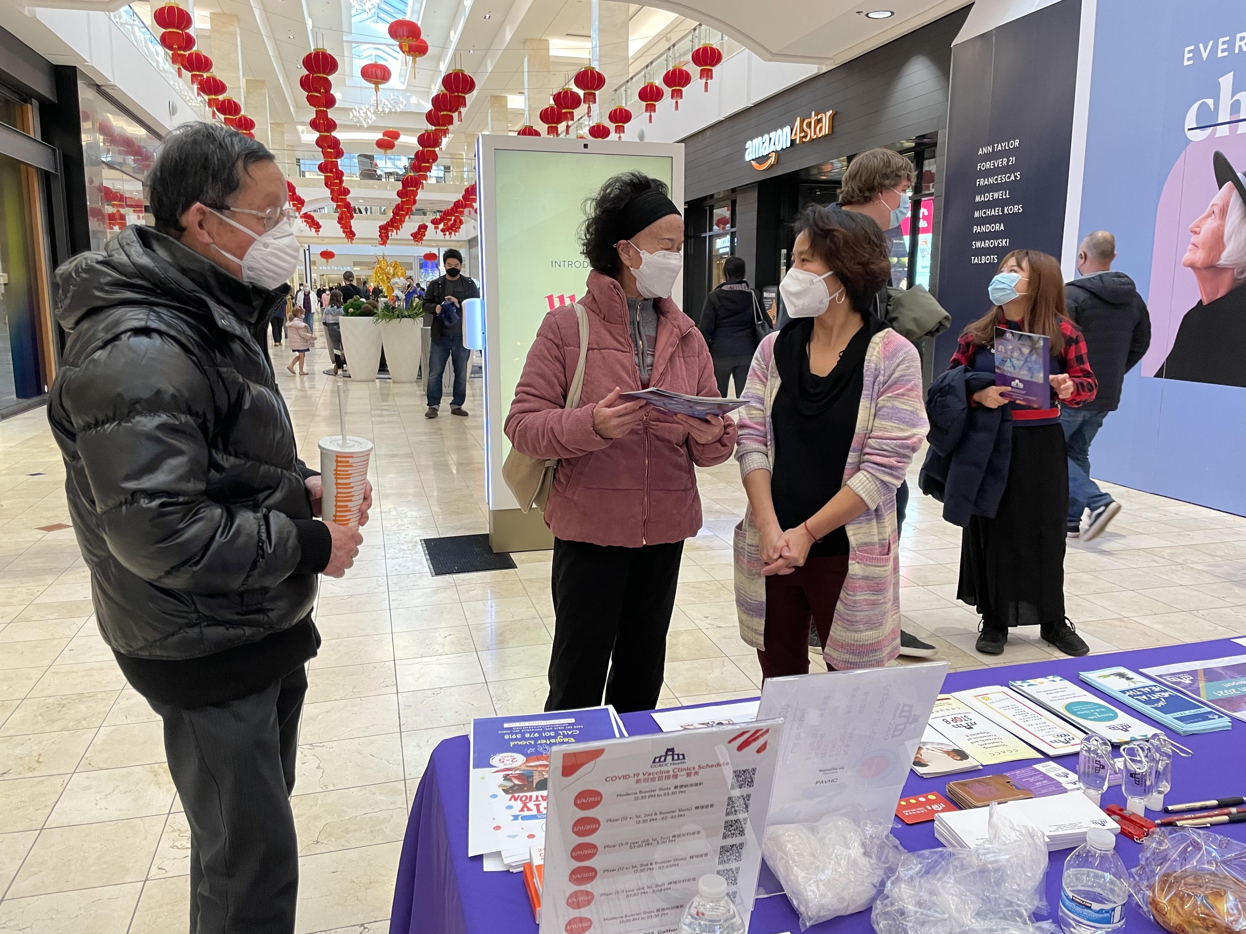 People wearing masks stand at an information booth located in a shopping center