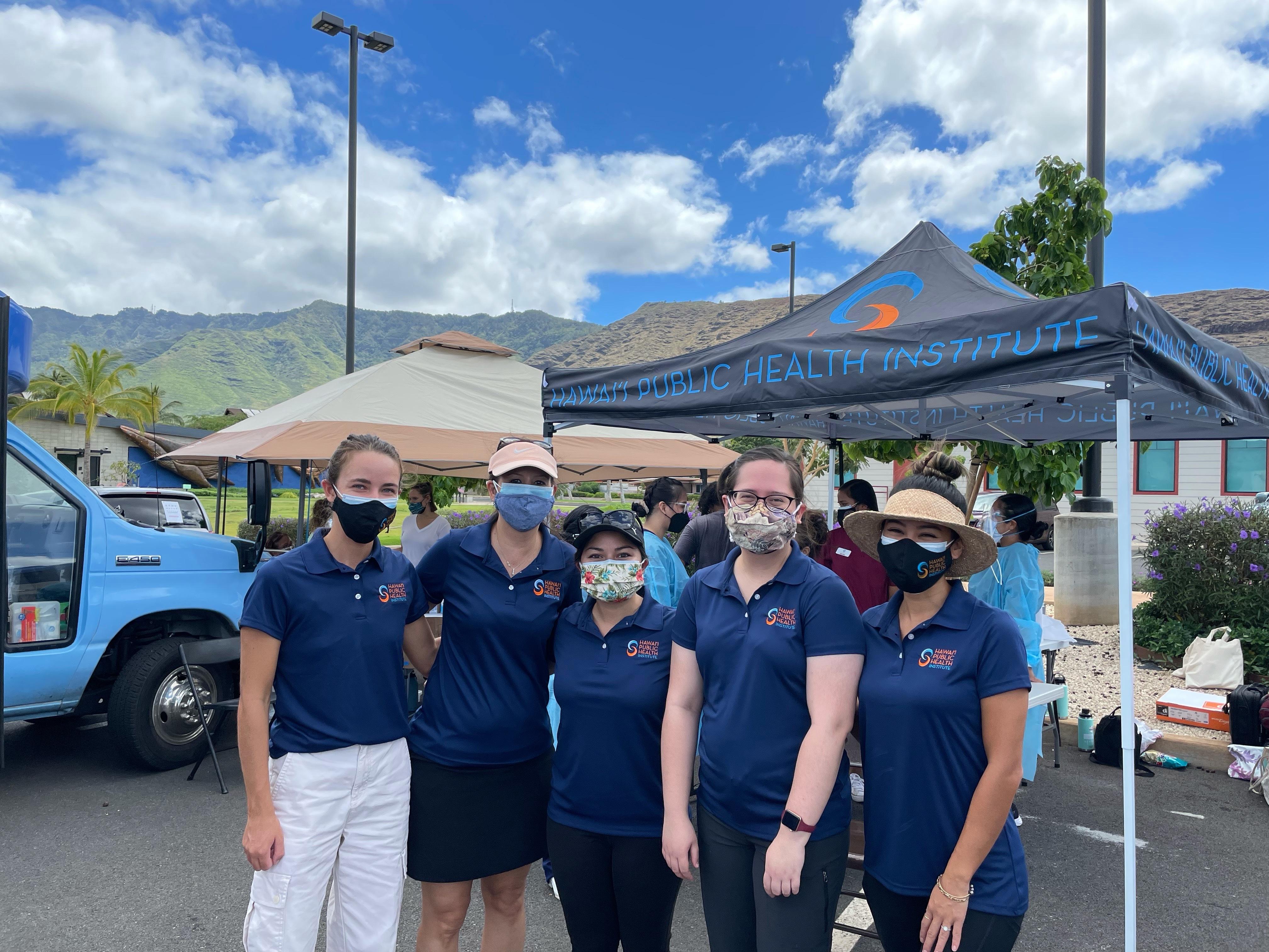 Five people wearing masks and matching navy blue shirts pose for a group picture