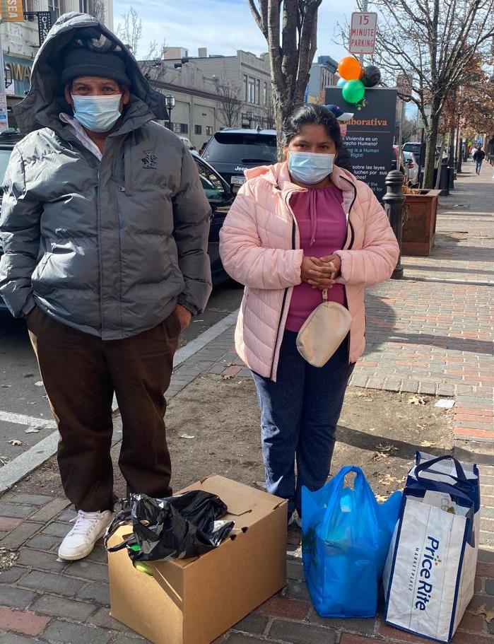 A couple stands outside with bags and boxes of supplies