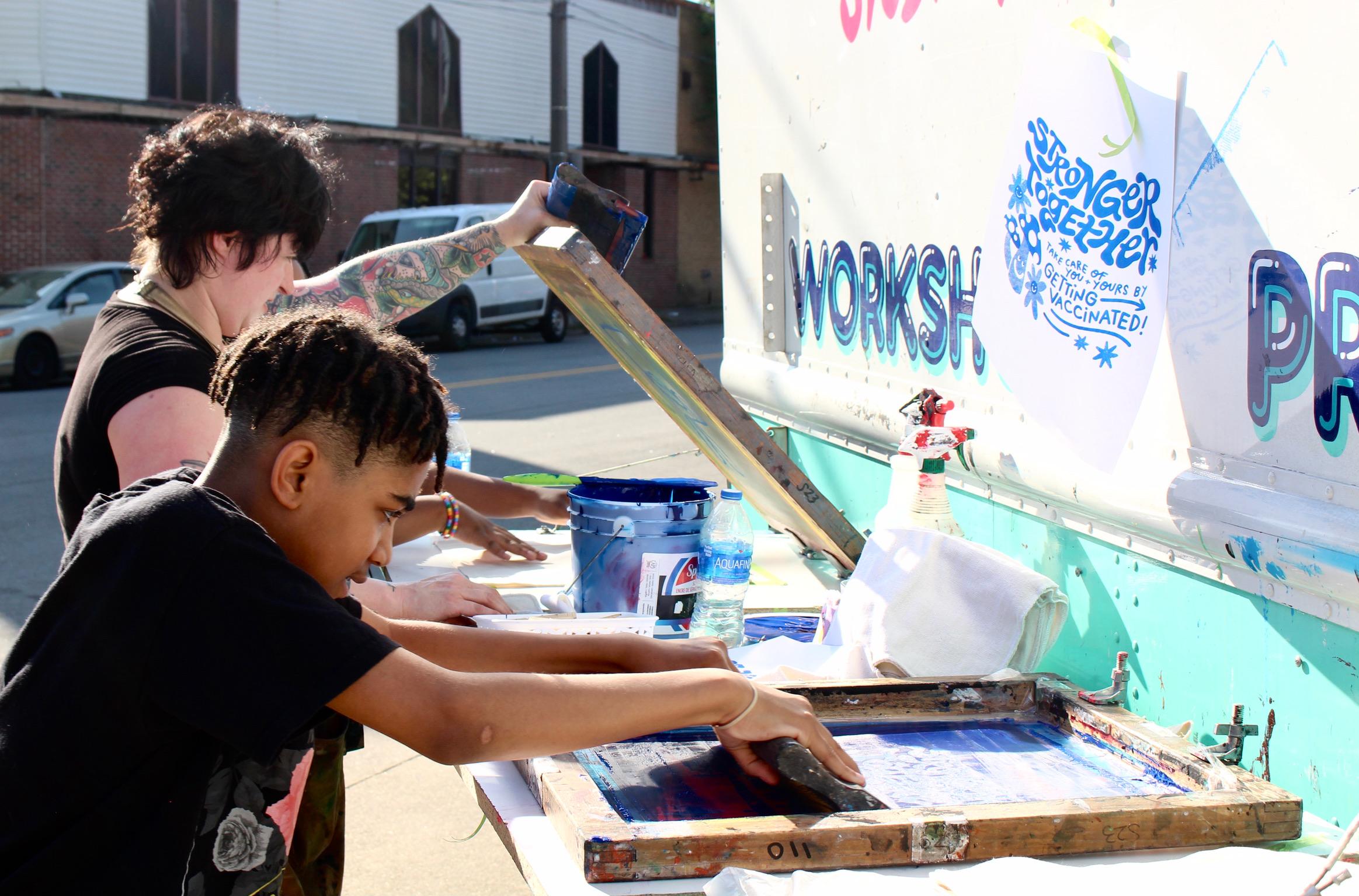 Two kids make a craft together at an outdoor fair