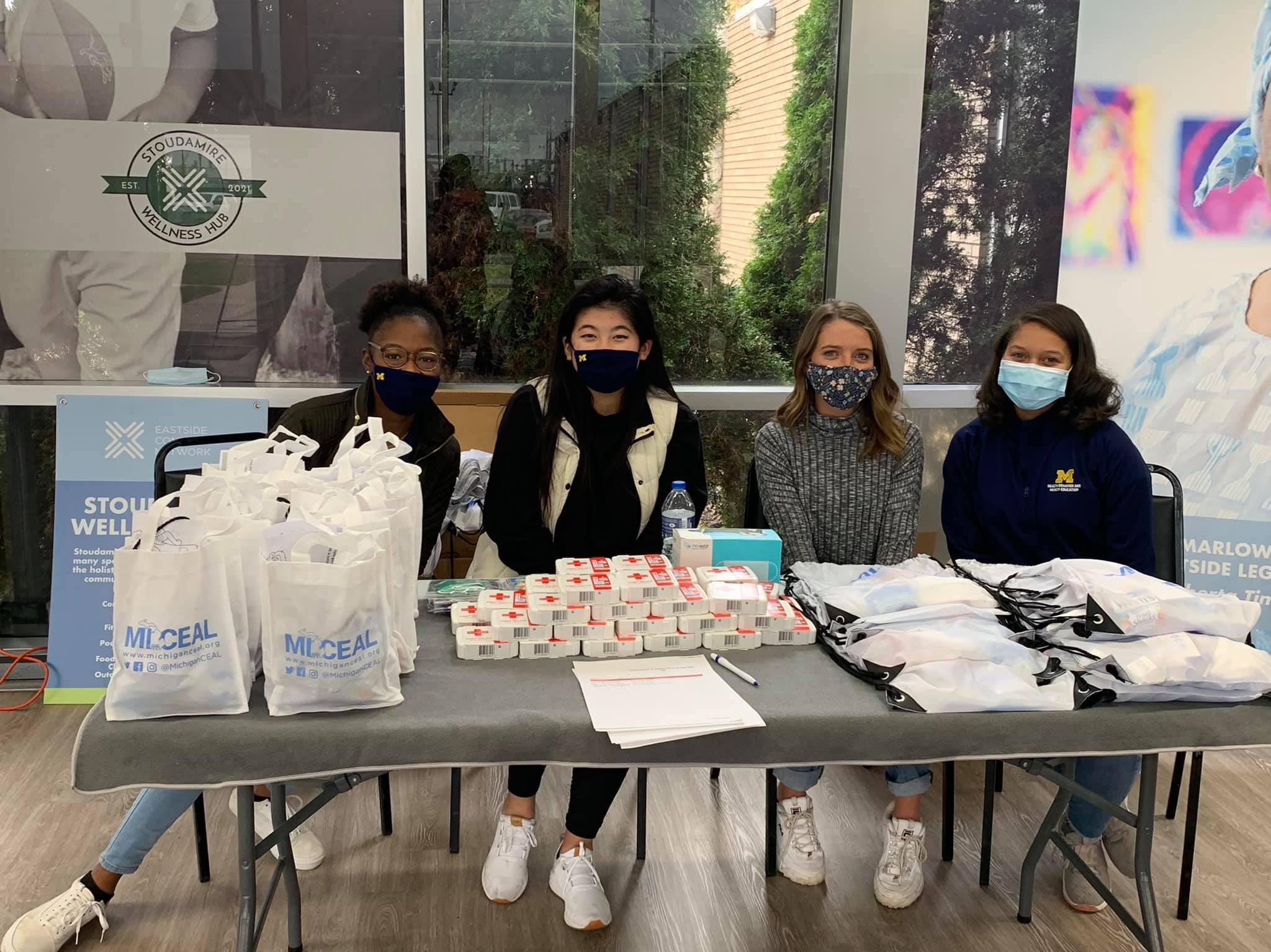 Four young women wearing masks sit at a volunteer table